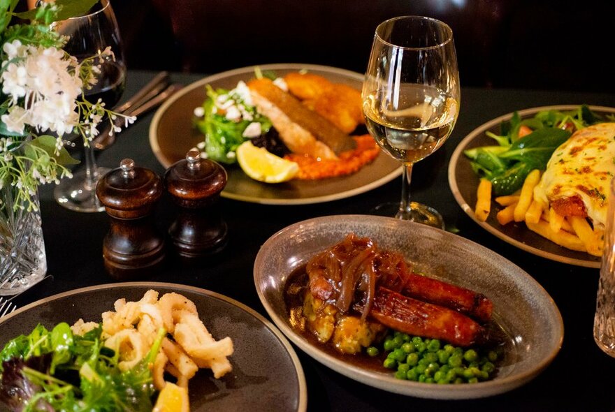 A table set with dishes of pub food and glasses of wine.