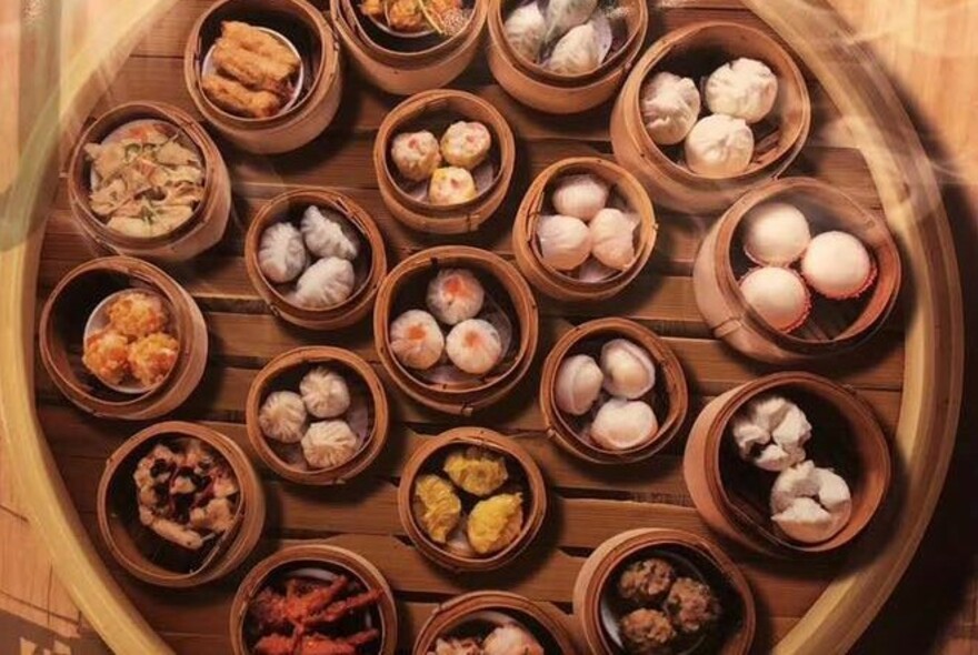 Wooden lazy Susan with bamboo steamers and bowls of dumplings.