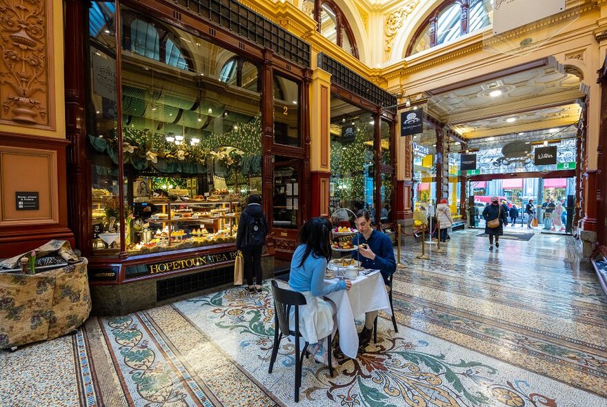 A couple dining on high tea on a small table in an arcade.