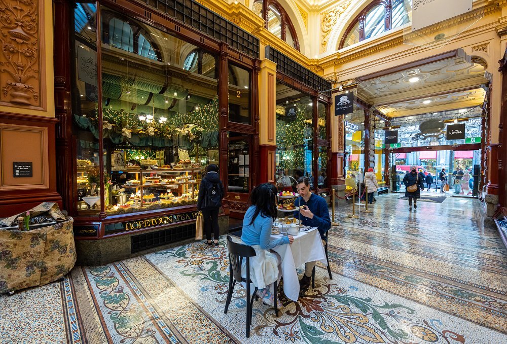A couple dining on high tea on a small table in an arcade.
