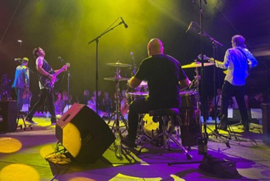 View from backstage of a band performing on stage to an audience.