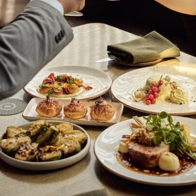 Plates of food on a restaurant table,  with a person's arm hovering over the top.