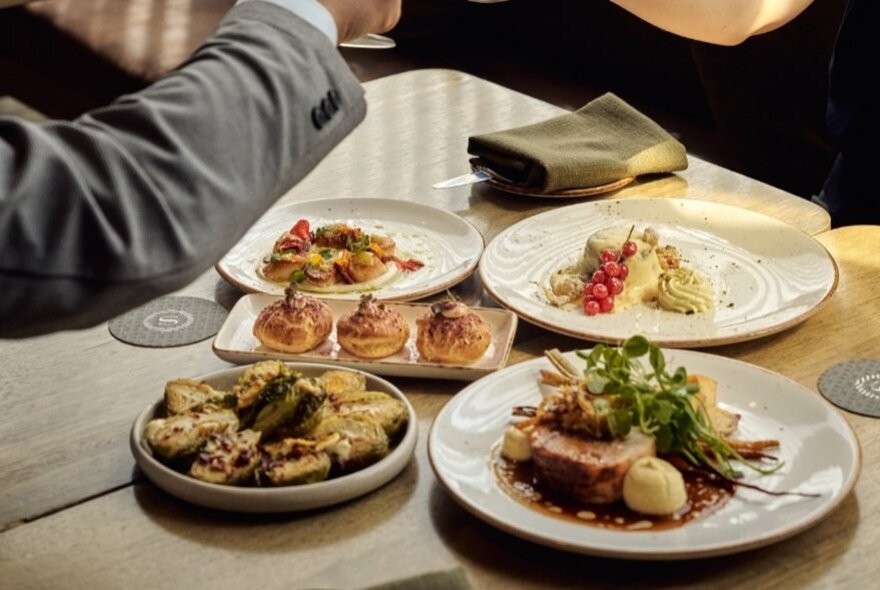 Plates of food on a restaurant table,  with a person's arm hovering over the top.
