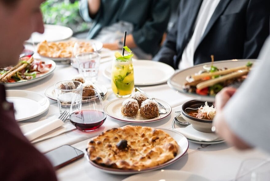 Patrons seated at a restaurant table with pizzas and drinks.