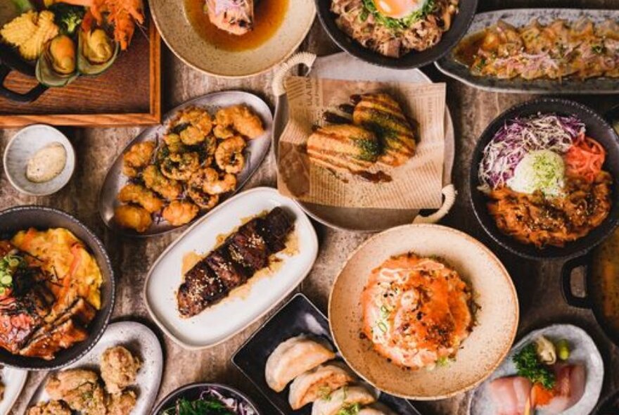 Overhead view of varied dishes of Japanese food arranged on a table in a restaurant.