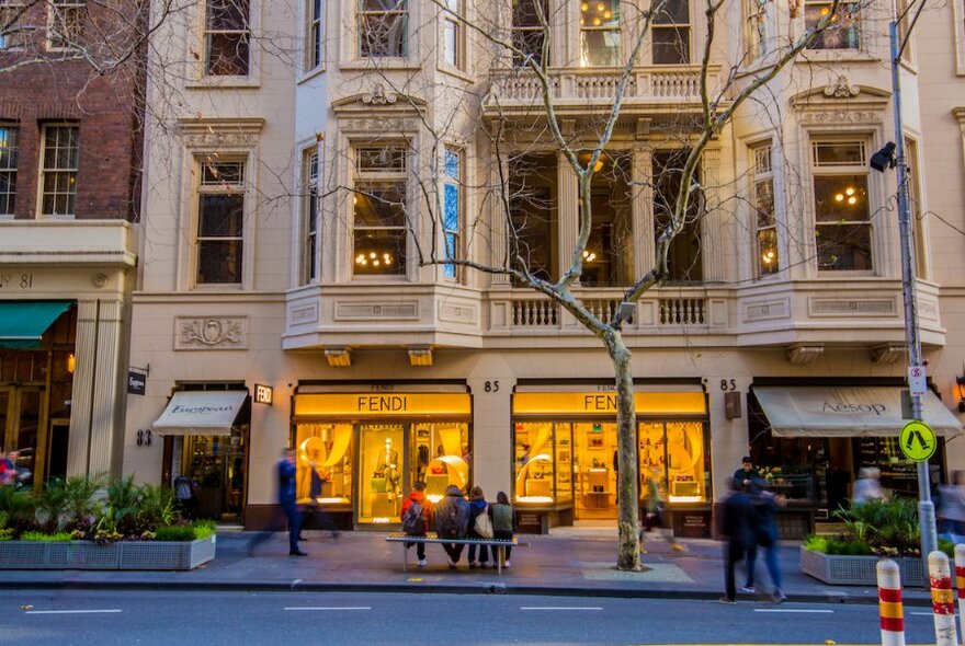 People sit on a bench outside the brightly lit windows of the Fendi store in Collins Street.