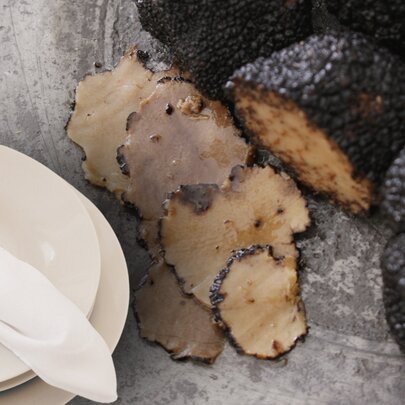 Sliced black truffles beside whole black truffles next to a small plate with a white napkin. 