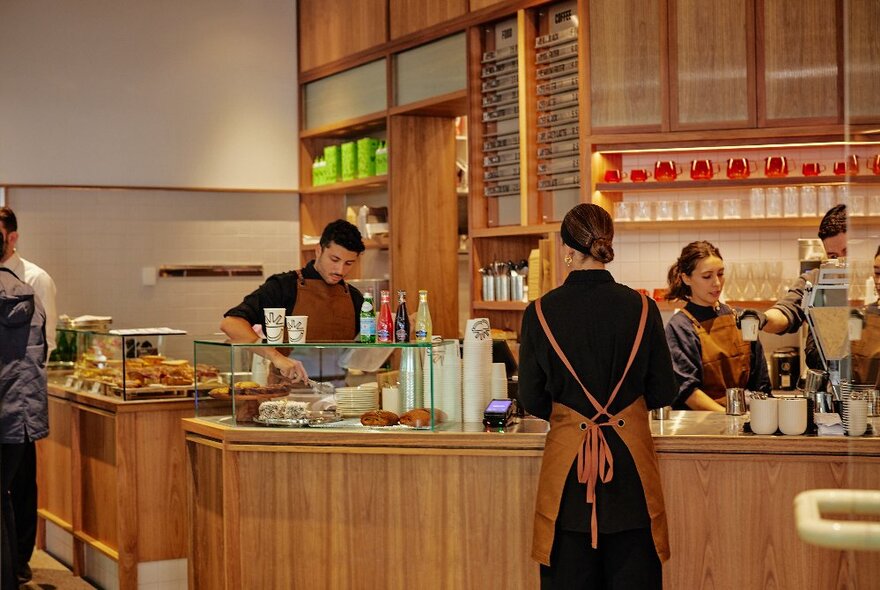 Interior of cafe, with staff working behind a sleek wooden counter and service area, with one of them making coffees.