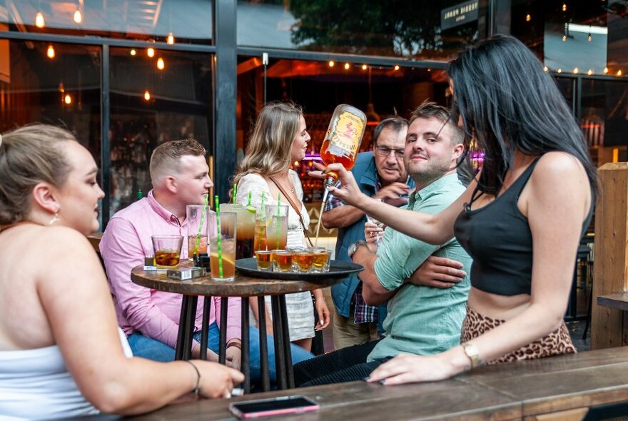 Woman pouring shots at an outside table, daylight.