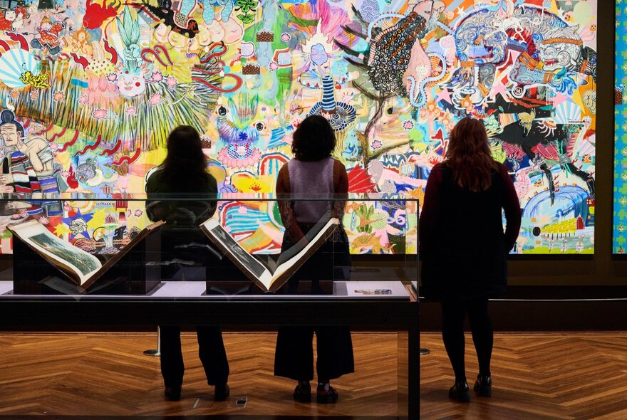 Silhouettes of three women looking at a large painting covering a wall in the State Library of Victoria.