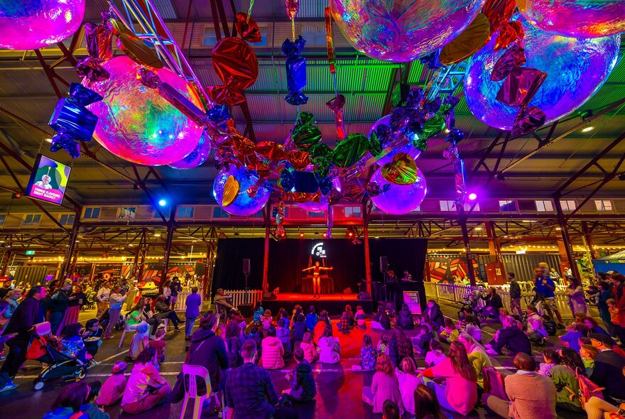 A performer on stage at a busy market under colourful lights and disco balls.