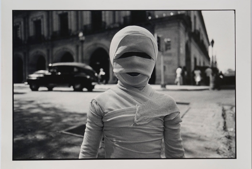 Vintage image of a child wrapped in bandages, including the face, a 1940s car and streetscape in the background.