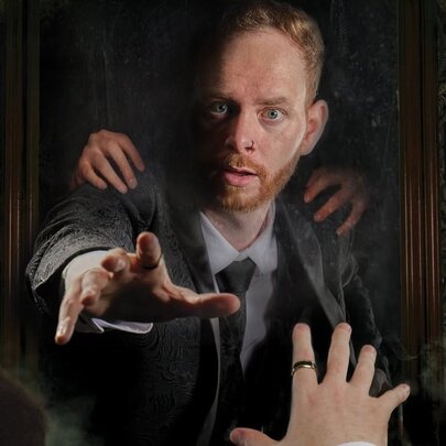 Mentalist and magician Jay Cristo reaching out with his hand from a picture frame, towards a hand reaching towards him from the foreground.