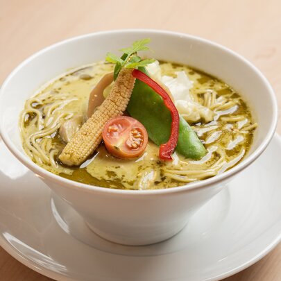 A bowl of creamy matcha chicken ramen with vegetables on top.