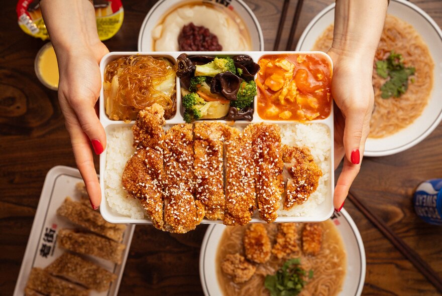 Hands holding trays of Asian-style meat and vegetables.