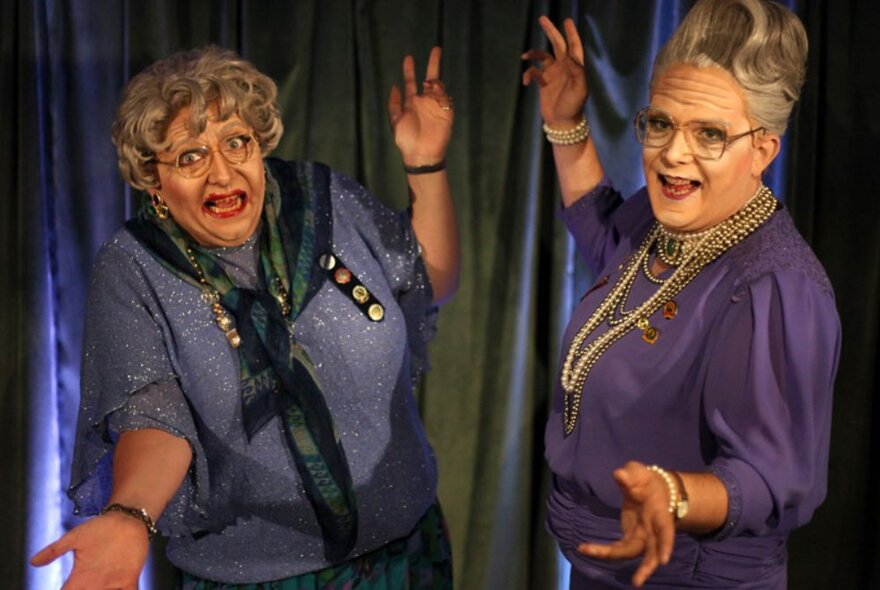 Two men dressed as elderly ladies wearing wigs and jewels.