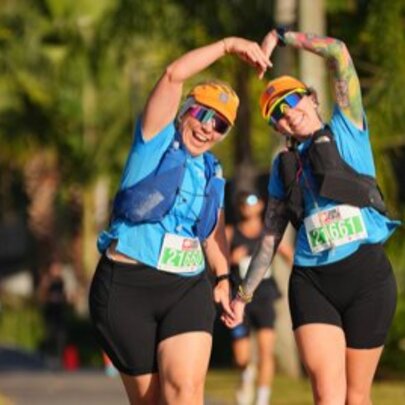 Two women leaning together and forming a heart with their arms during a charity fun run. 