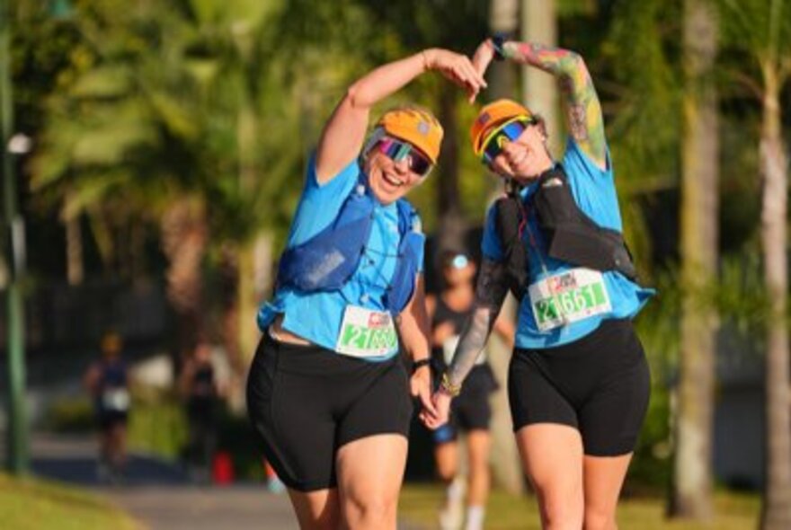 Two women leaning together and forming a heart with their arms during a charity fun run. 