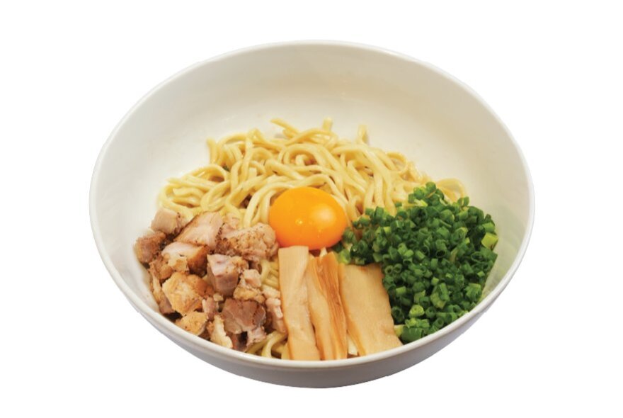 A white bowl of ramen from the Japanese chain Machida Shoten, with chopped meat, an egg yolk, shopped green spring onions and noodles.