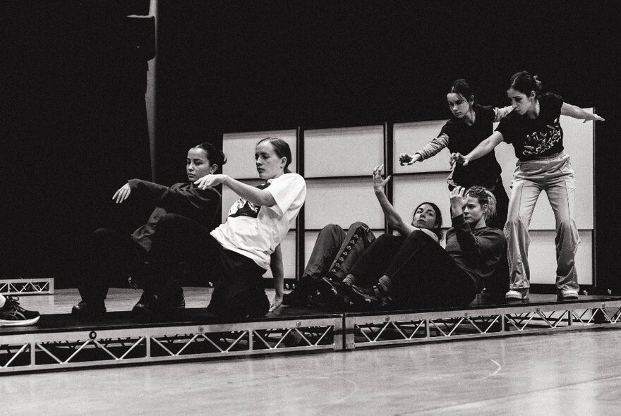 Six people dancing on a slightly raised platform in a large studio space; black and white image.