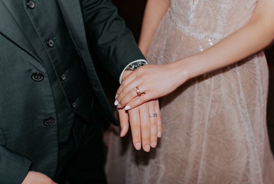 A man and woman's hands touching, each wearing wedding bands.