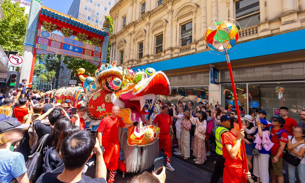 A large Chinese dragon is parading down Chinatown with a crowd of people watching on