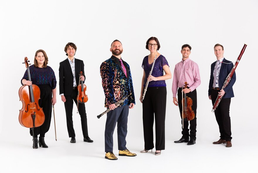 The six musicians of the Inventi Ensemble, standing against a white background and all holding musical instruments.