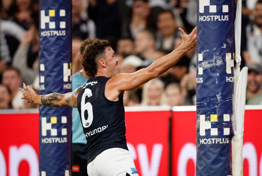 A Carlton footballer celebrates in front of goal with arms outstretched. 