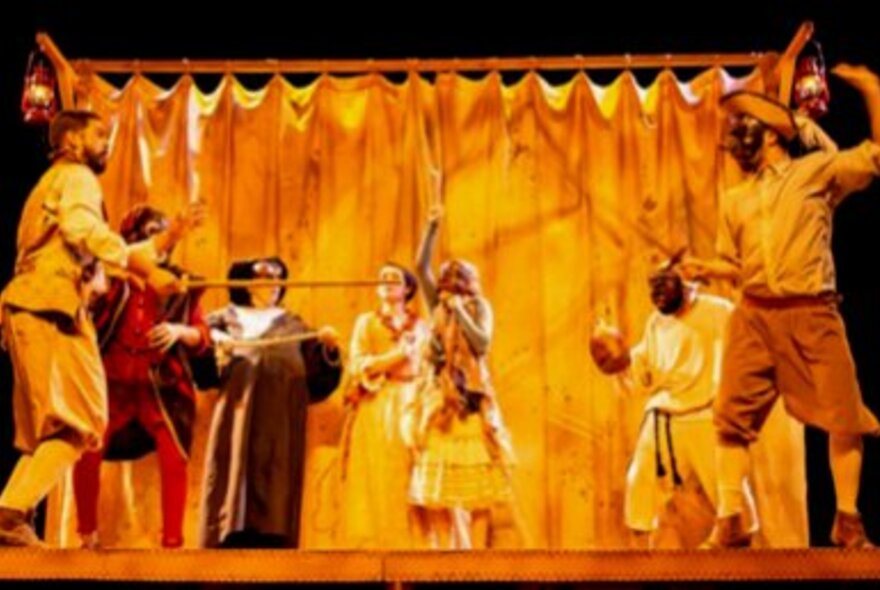 A performance on stage with actors, using Commedia dell’Arte masks and props.