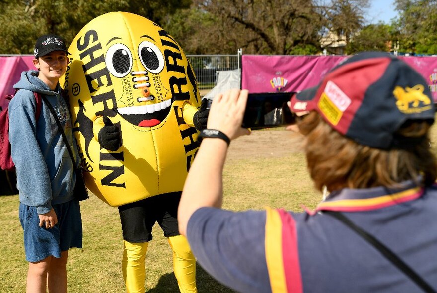 Person having their photo taken next to a lifesize yellow Sherrin football mascot.