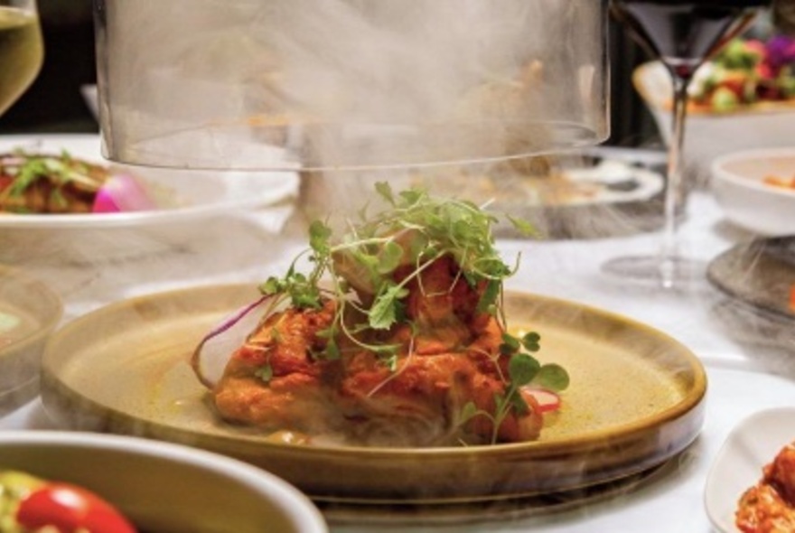 A Nepalese curry served on an eathenware dish with a glass cloche that has just been removed.