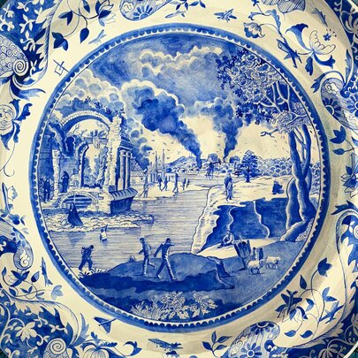 A delicately painted porcelain plate with a blue design depicting waves around the outside and a burning landscape in the centre.
