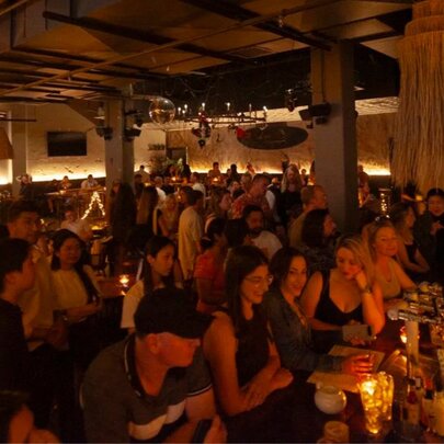 Crowded, dimly lit beer with people crowded around the bar and dance floor.