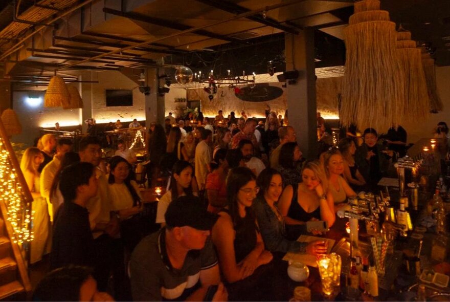 Crowded, dimly lit beer with people crowded around the bar and dance floor.
