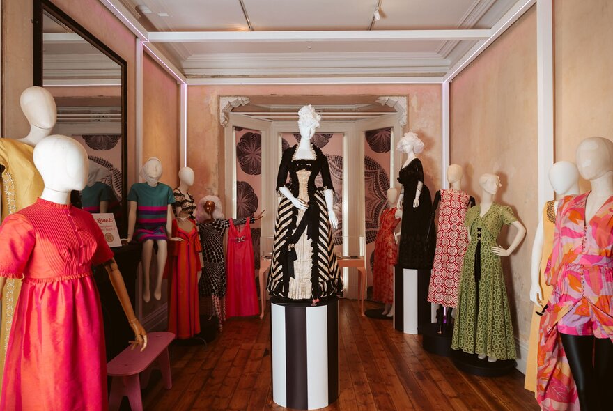 Colourful and bold dresses from different eras, on faceless clothing mannequins, on exhibition in a large room.