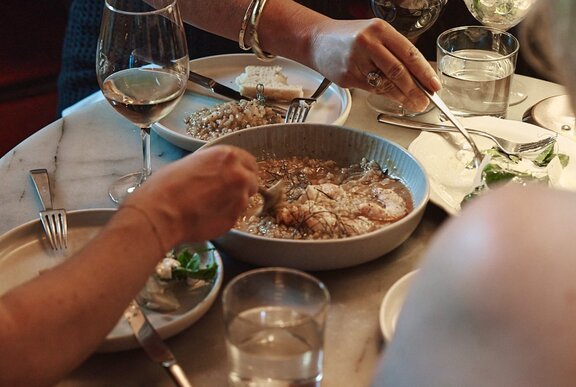 A busy table setting with a large share plate of stew in the middle of four diners