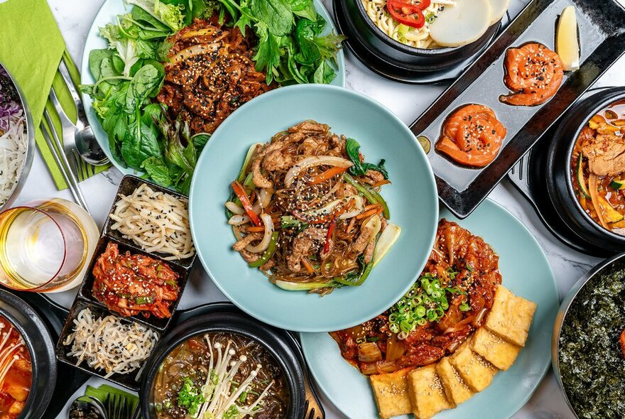 Looking down on a table packed with various Korean dishes.