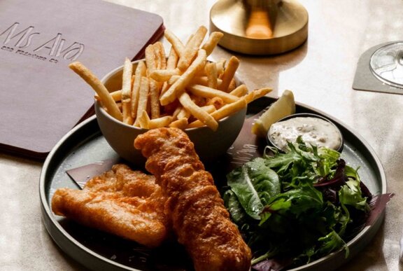 Beer battered fish and shoestring fries, plus salad on a dark plate on a table.