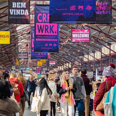 A crowded scene within the Queen Victoria Market, featuring various banners for a craft fair and market called 'CRFT*WRK'
