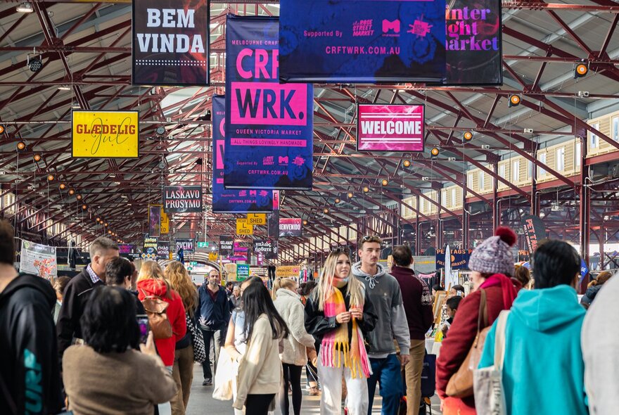 A crowded scene within the Queen Victoria Market, featuring various banners for a craft fair and market called 'CRFT*WRK'