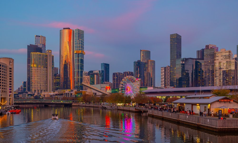 A view of a river at sunset with a Ferris wheel and a city skyline in the background.