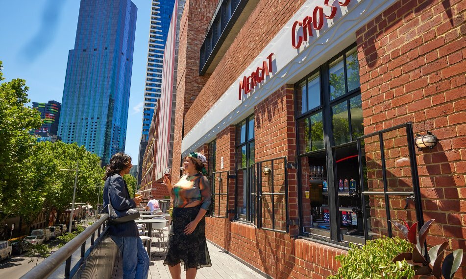 Two people enjoying a drink on a bar balcony in the city.