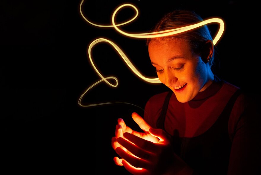 A person looking down at their cupped hands, light radiating up onto their face from their hands, and swirling around them in a curved streak.