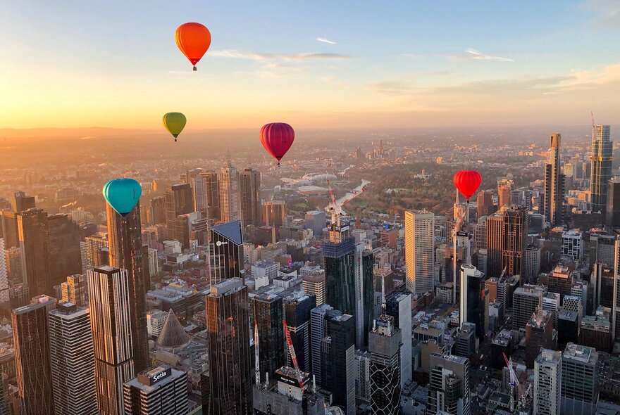Colourful hot air balloons flying over Melbourne city buildings at sunrise.