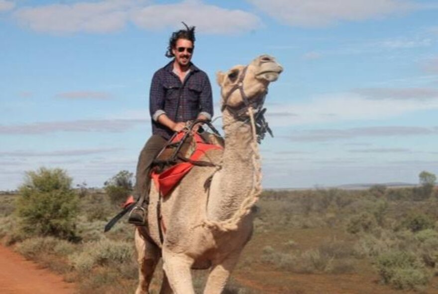 A man riding a camel in outback Australia.
