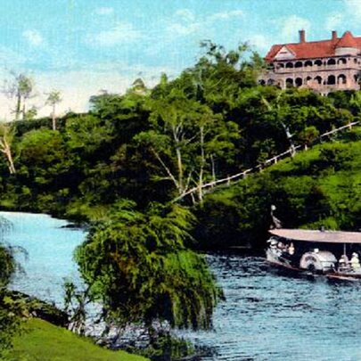 A ferry on the Yarra River, a green hilly bank and a stately building on one side, captured in a vintage tinted postcard format. 