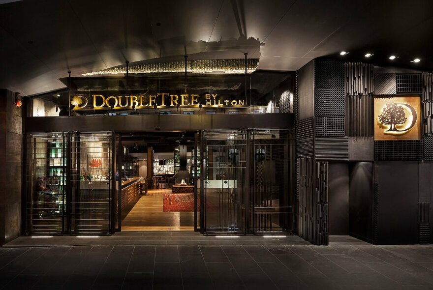 The street entrance to Double Tree by Hilton showing the lobby, and signage above the large glass doors.