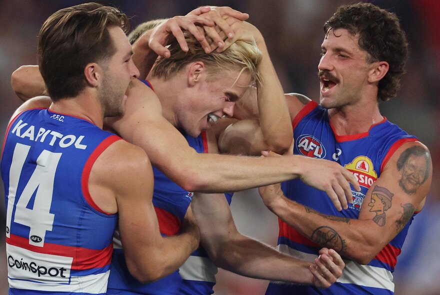 Several Western Bulldogs AFL football players  hugging each other on the football field.