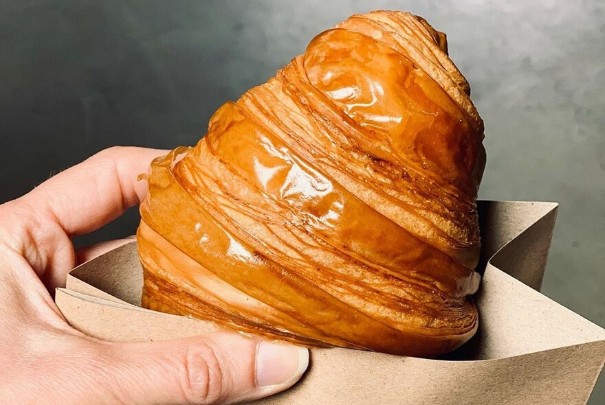 Person holding a takeaway croissant in a bag.