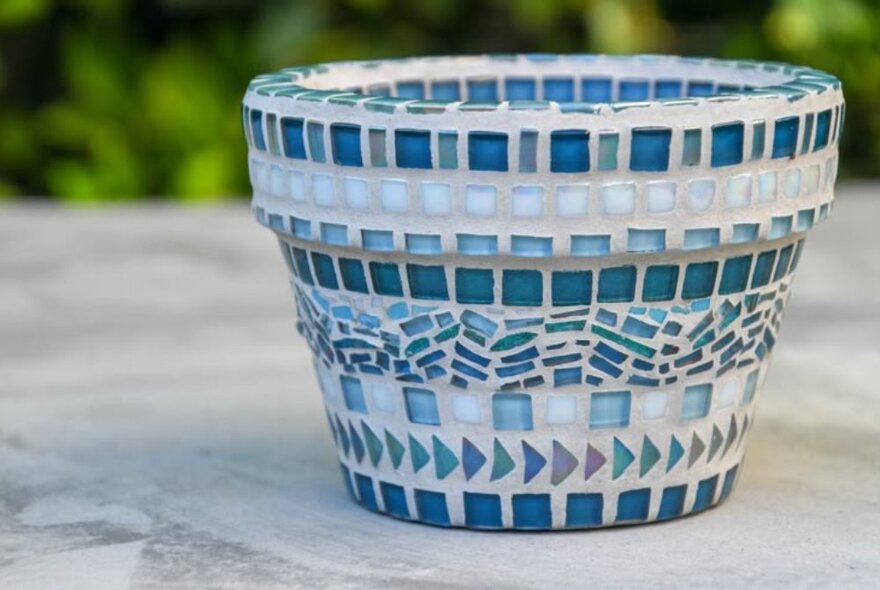 A blue planter pot with rows of coloured tiles.